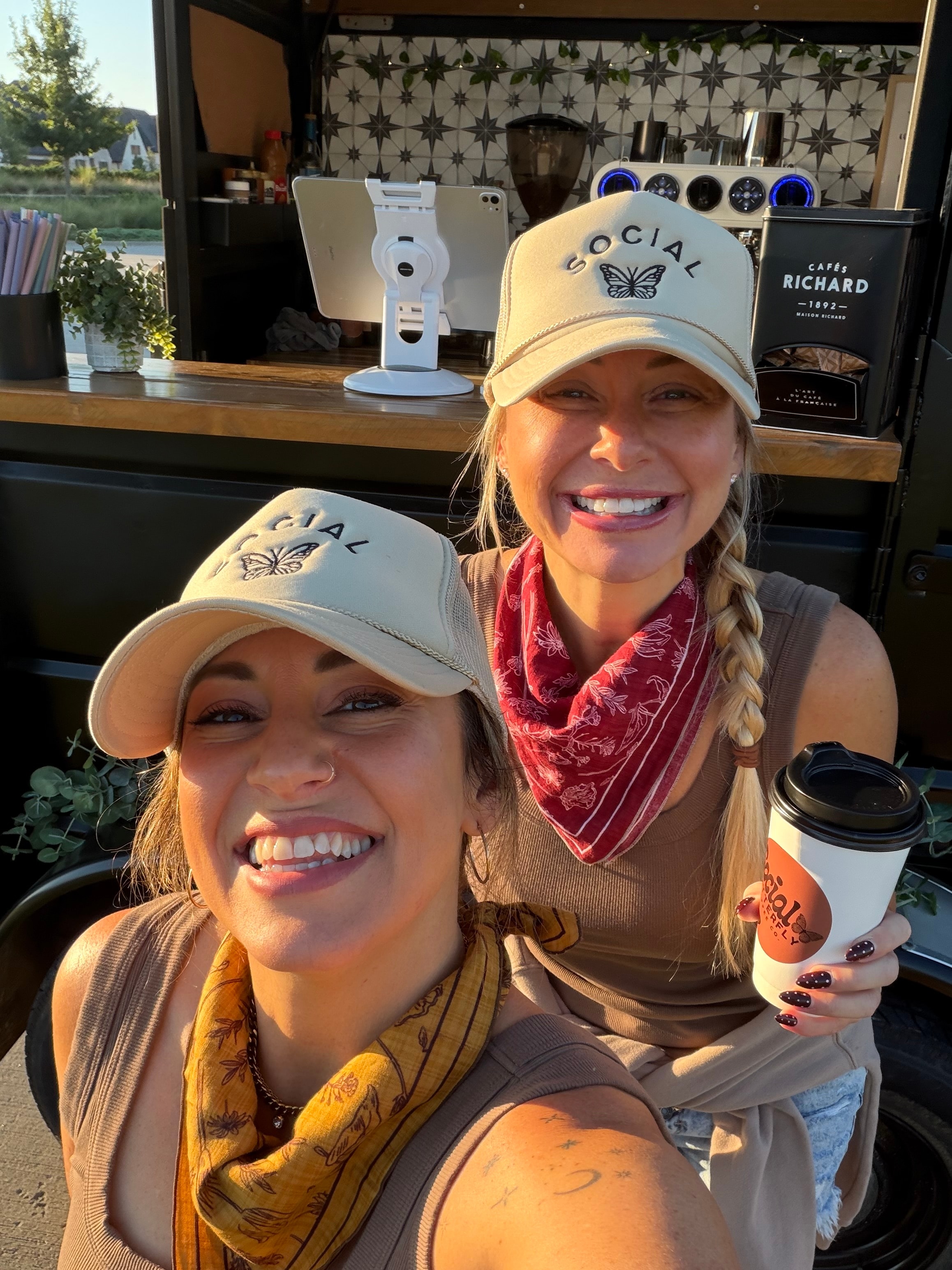 Two baristas in Social Butterfly hats smiling at a popup event